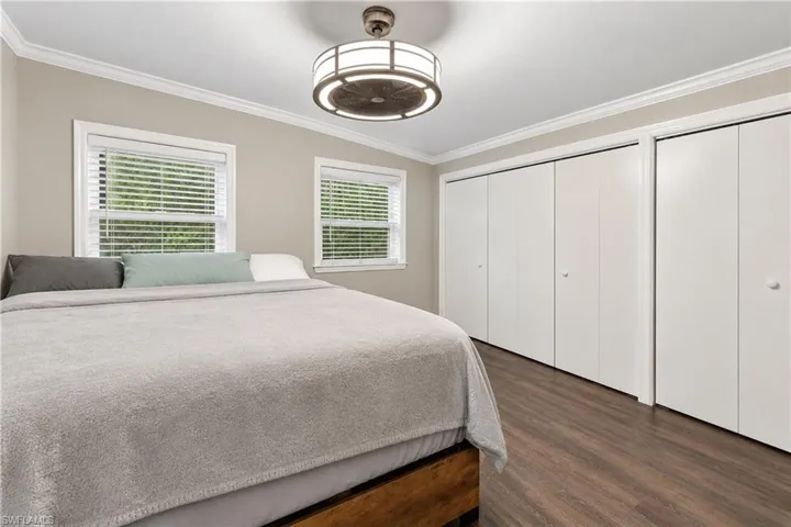 Wood-finish flooring with crown molding, two windows with blinds, and white bi-fold closet doors bedroom number two features wall-to-wall closet space.