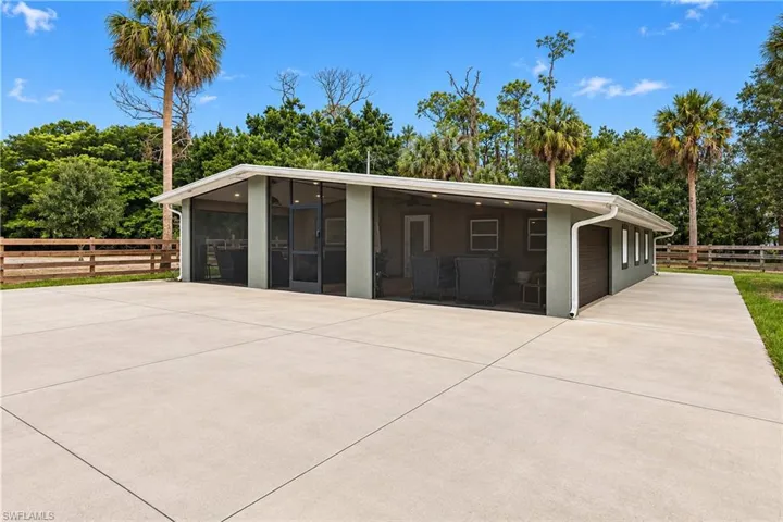 Expansive concrete paving with a screened outdoor living area, and surrounding wooden fence and wide side concrete walkway between front pasture and back pasture
