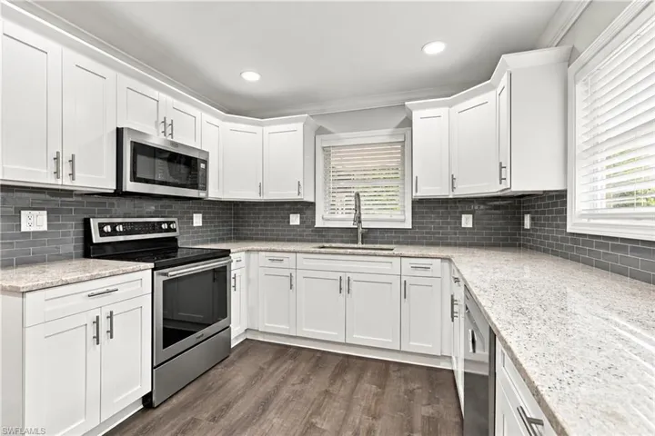 White cabinetry with brushed nickel hardware, light-toned granite countertops, gray subway tile backsplash, stainless steel appliances, and wood-finish flooring double bank kitchen window allows plenty of light into the kitchen.