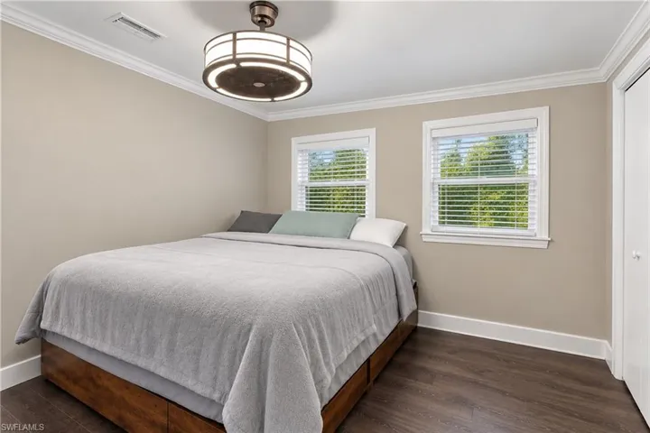 Crown molding, wood-finish flooring, two windows with blinds, and a flush-mount ceiling light fixture