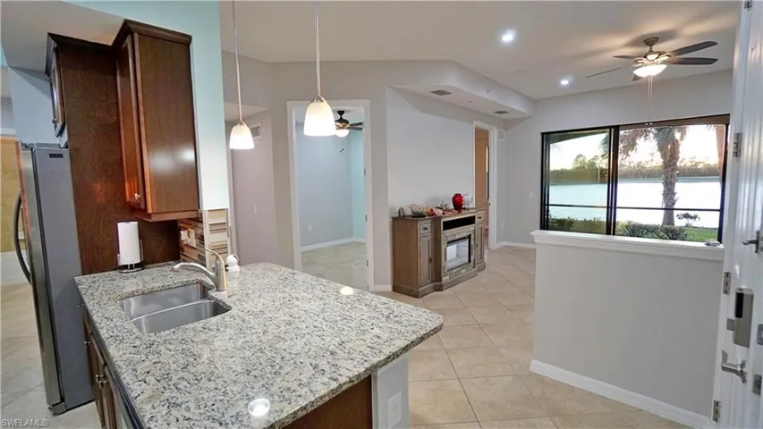 Kitchen featuring ceiling fan, sink, light stone countertops, stainless steel fridge, and decorative light fixtures