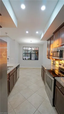 Kitchen with light stone countertops, an inviting chandelier, decorative light fixtures, decorative backsplash, and appliances with stainless steel finishes