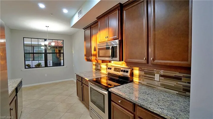 Kitchen featuring light stone counters, a notable chandelier, backsplash, light tile patterned flooring, and appliances with stainless steel finishes