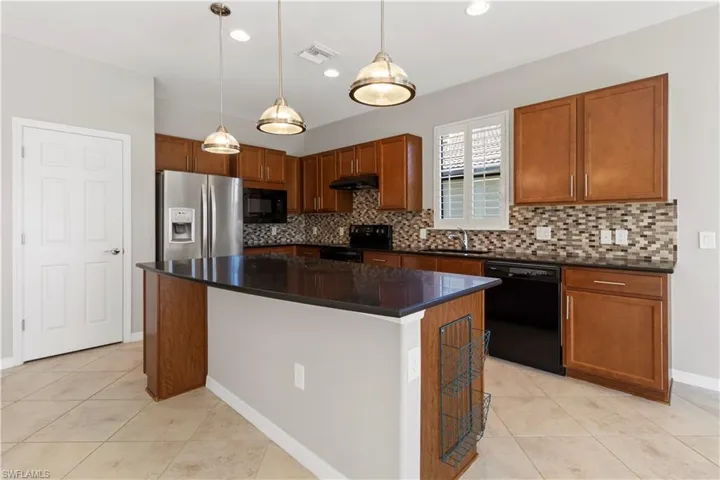 Kitchen featuring brown cabinetry, black appliances, decorative light fixtures, a kitchen island, and light tile patterned floors