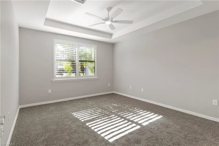 Carpeted spare room with a tray ceiling and ceiling fan