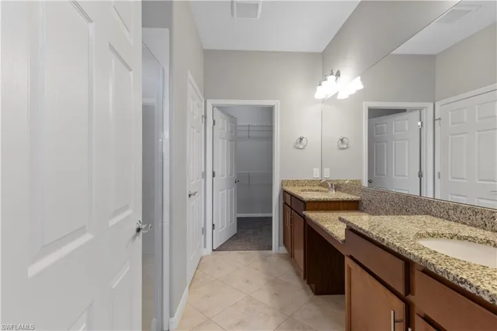Bathroom with double vanity, a spacious closet, and light tile patterned floors