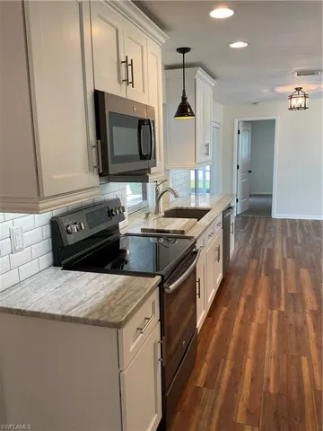 Kitchen featuring decorative backsplash, dark wood-style floors, white cabinetry, dishwashing machine, and stove