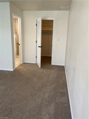 Unfurnished bedroom featuring a walk in closet, baseboards, carpet floors, ensuite bathroom, and a closet