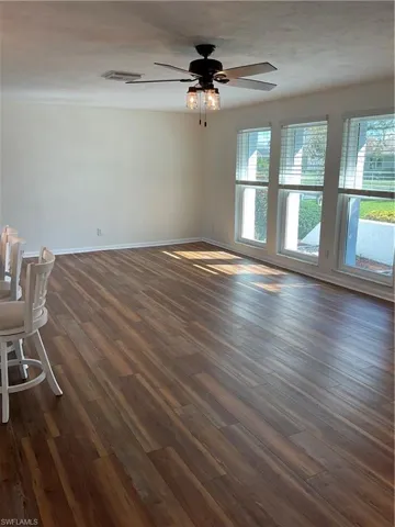 Unfurnished room with a wealth of natural light, visible vents, dark wood-style floors, and a ceiling fan
