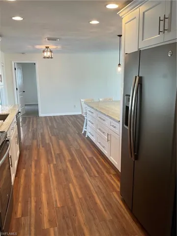 Kitchen with dark wood-type flooring, light stone countertops, white cabinetry, fridge, and range