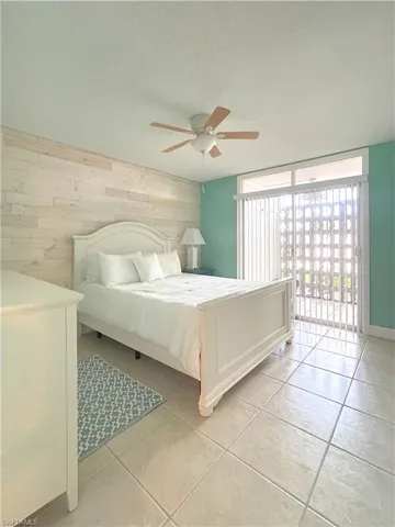 Bedroom with wood walls, access to exterior, light tile patterned floors, a textured ceiling, and ceiling fan