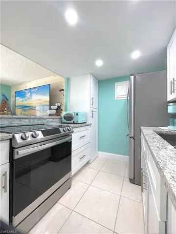 Kitchen featuring appliances with stainless steel finishes, white cabinetry, light tile patterned floors, light stone counters, and recessed lighting