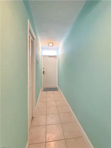 Hallway featuring a textured ceiling and light tile patterned floors