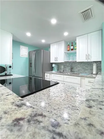 Kitchen featuring stainless steel fridge with ice dispenser, light stone counters, open shelves, tasteful backsplash, and recessed lighting