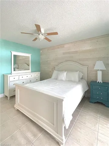 Bedroom featuring light tile patterned floors, wooden walls, a textured ceiling, and ceiling fan