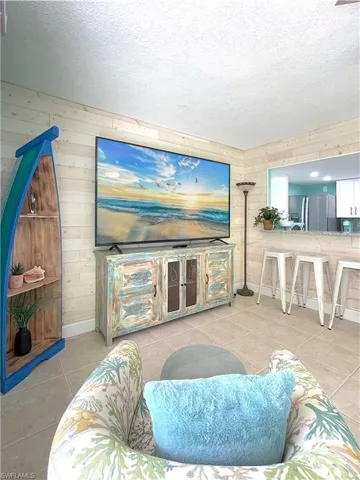 Living area with wooden walls, light tile patterned flooring, and a textured ceiling