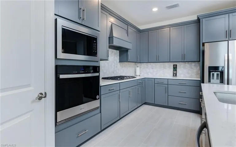 Kitchen with stainless steel appliances, light stone counters, decorative backsplash, and recessed lighting