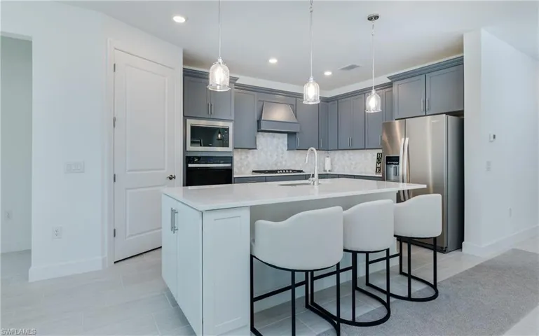 Kitchen with stainless steel appliances, an island with sink, gray cabinetry, pendant lighting, and tasteful backsplash