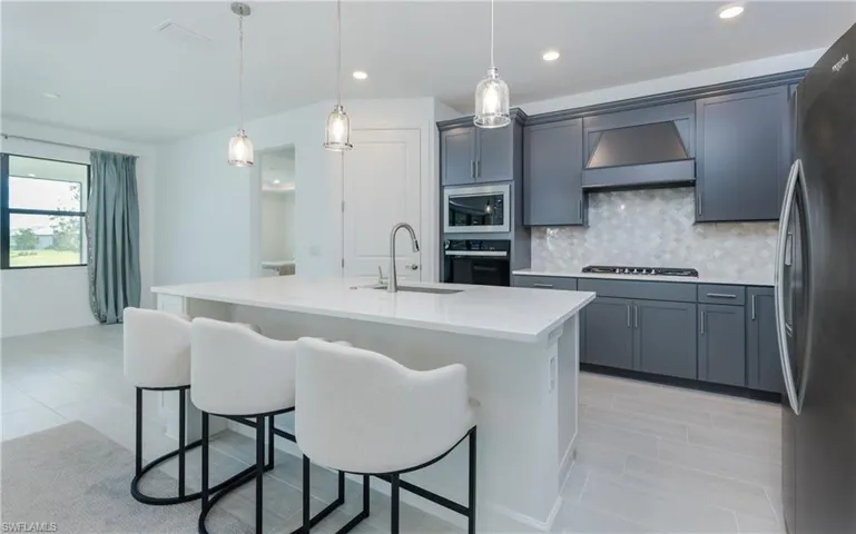 Kitchen with stainless steel appliances, a breakfast bar, light stone countertops, a kitchen island with sink, and hanging light fixtures