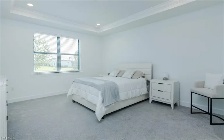 Bedroom with light colored carpet, ornamental molding, recessed lighting, and a tray ceiling