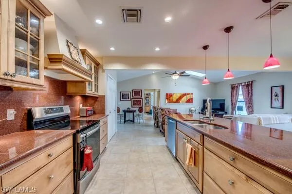 Kitchen with decorative backsplash, hanging light fixtures, stainless steel appliances, sink, and lofted ceiling with skylight