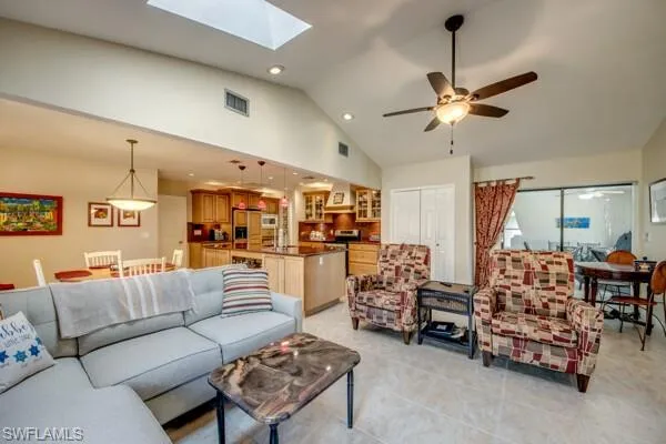 Living room featuring ceiling fan, high vaulted ceiling, a skylight, and light tile patterned floors