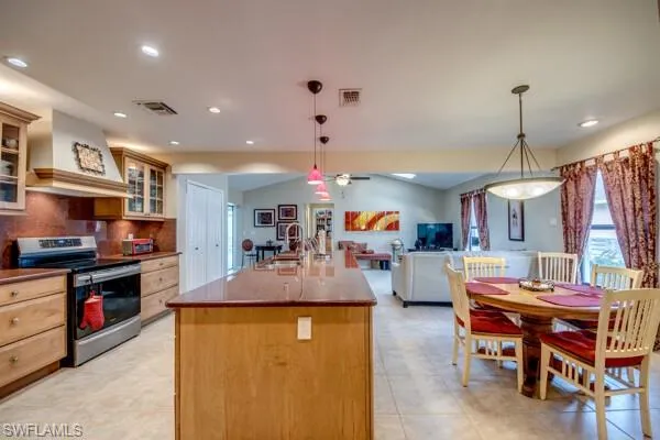 Kitchen featuring a kitchen island with sink, stainless steel range with electric stovetop, sink, pendant lighting, and premium range hood