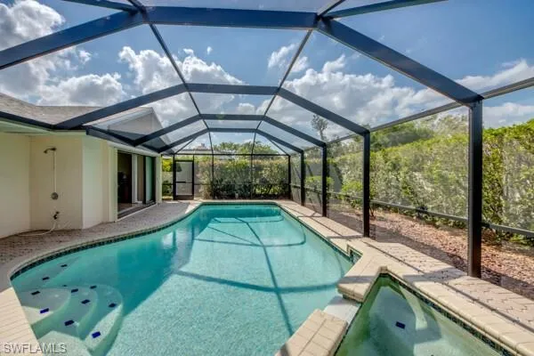 View of pool with an in ground hot tub, a patio, and glass enclosure