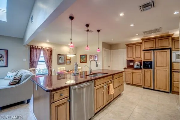 Kitchen featuring built in appliances, an island with sink, dark stone countertops, sink, and pendant lighting