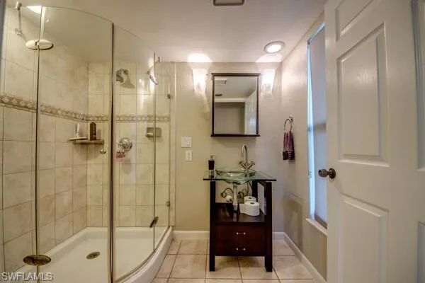 Bathroom with a shower with shower door, tile patterned floors, and sink