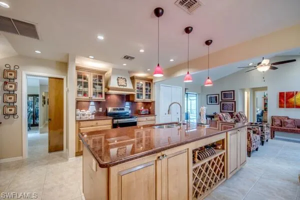 Kitchen with stainless steel stove, a center island with sink, sink, decorative light fixtures, and custom exhaust hood