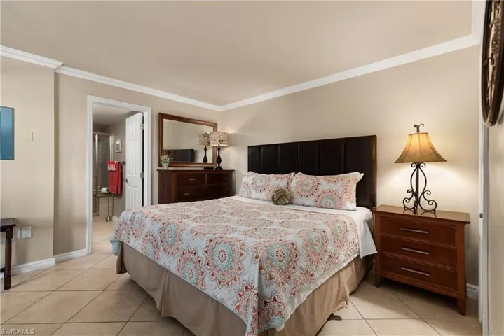 Bedroom featuring crown molding, light tile flooring, and ensuite bath