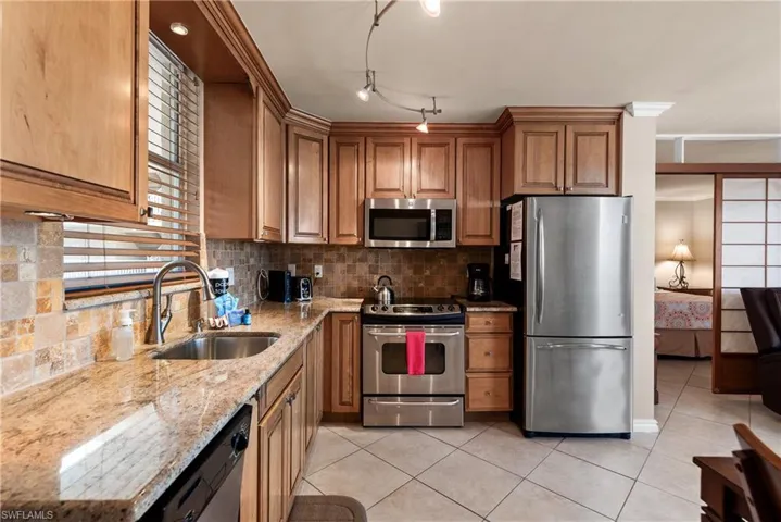 Kitchen with stainless steel appliances, light granite countertops, light tile floors, warm wood cabinets, and decorative backsplash