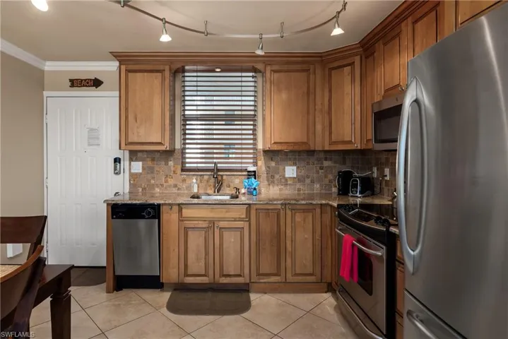 Kitchen with stainless steel appliances, light stone countertops, tasteful backsplash, wood cabinets, and crown molding
