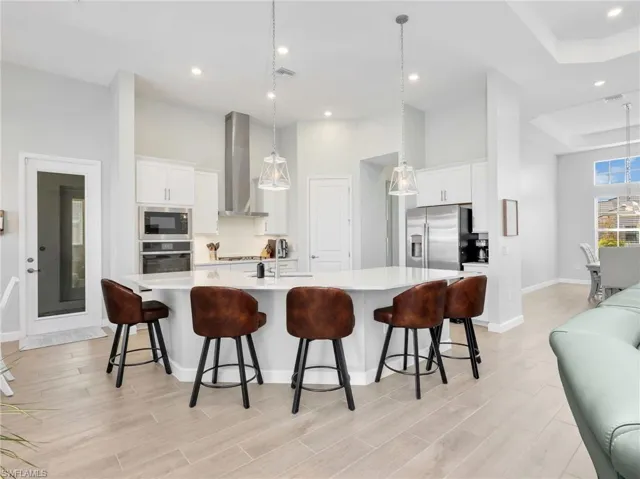 Kitchen featuring white cabinets, hanging light fixtures, a high ceiling, and a kitchen bar