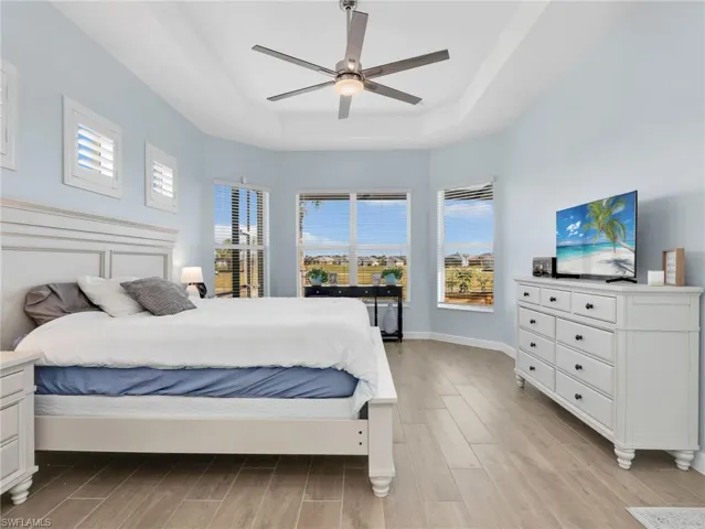 Bedroom with wood finish floors, a ceiling fan, a raised ceiling, and multiple windows