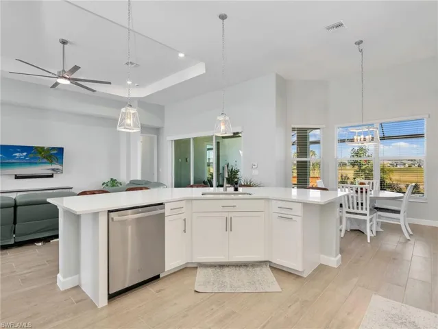 Kitchen with stainless steel dishwasher, light wood-style floors, pendant lighting, an island with sink, and a raised ceiling