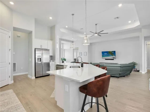 Kitchen featuring hanging light fixtures, stainless steel appliances, a breakfast bar, white cabinets, and light wood-style flooring