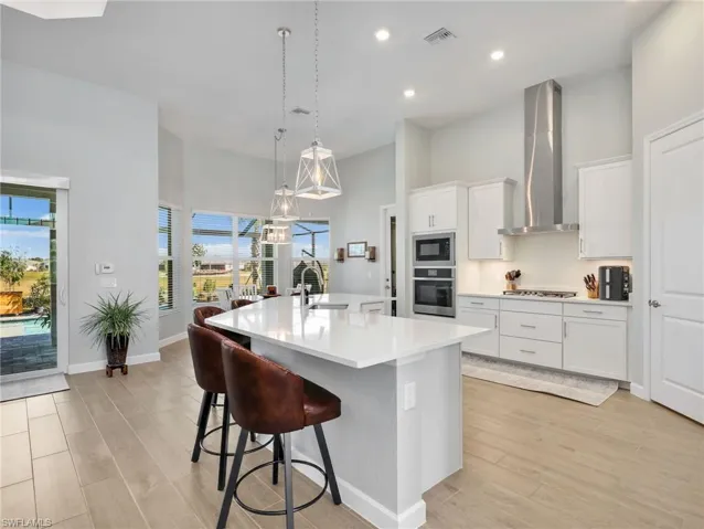 Kitchen featuring a high ceiling, pendant lighting, light wood-style floors, white cabinets, and a center island with sink