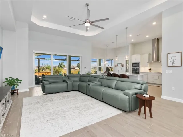 Living area featuring ceiling fan, a high tray ceiling, wood finish floors, and recessed lighting
