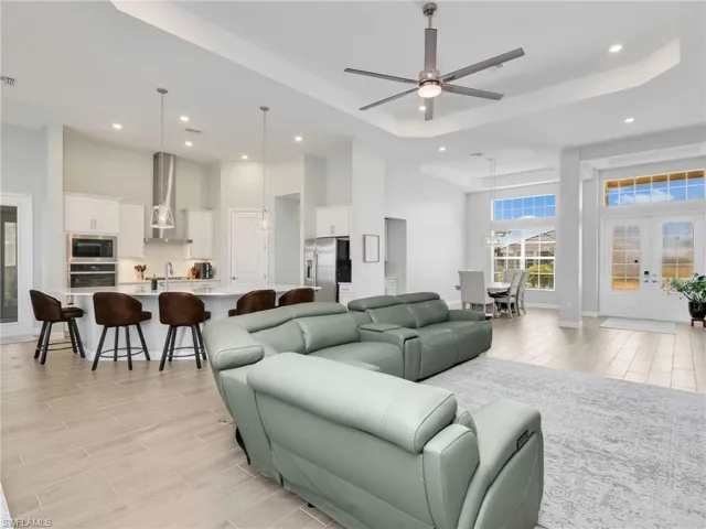 Living room with a ceiling fan, a high tray ceiling, recessed lighting, wood finish floors, and french doors