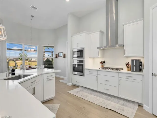 Kitchen with white cabinets, stainless steel appliances, a high ceiling, light wood-style flooring, and light stone countertops