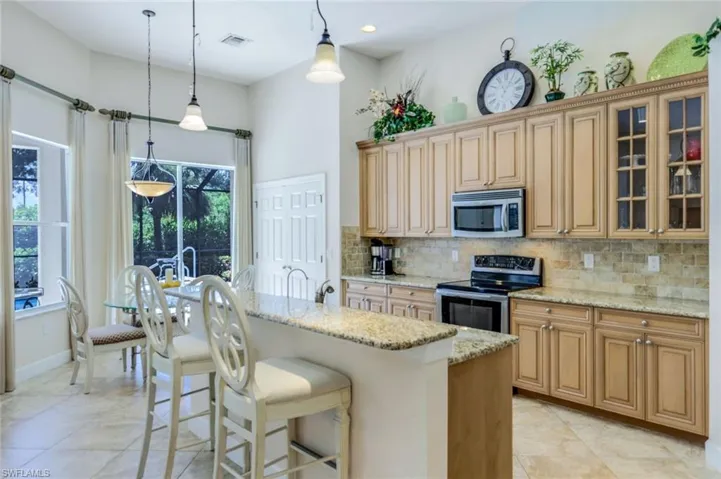 Kitchen featuring light tile patterned floors, backsplash, light stone counters, appliances with stainless steel finishes, and pendant lighting