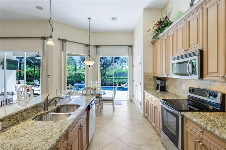 Kitchen with tasteful backsplash, light stone counters, appliances with stainless steel finishes, and sink