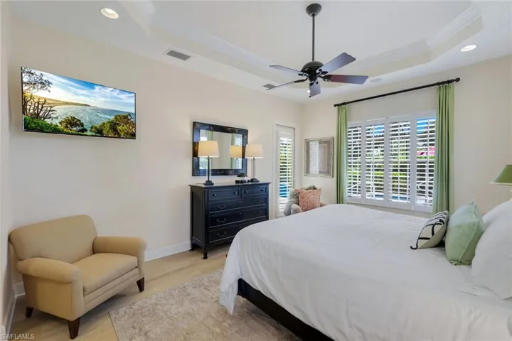 Bedroom with crown molding, ceiling fan, light wood-type flooring, and a tray ceiling