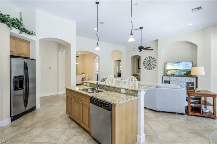 Kitchen with light tile patterned floors, an island with sink, stainless steel appliances, light stone countertops, and sink