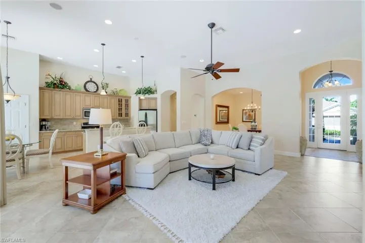 Tiled living room with ceiling fan with notable chandelier and a towering ceiling