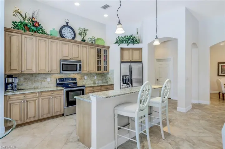Kitchen featuring a breakfast bar, a high ceiling, backsplash, light stone countertops, and appliances with stainless steel finishes