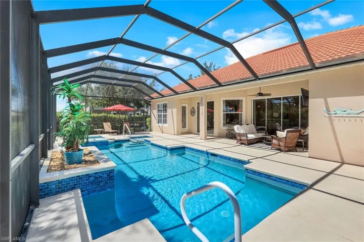 View of pool with glass enclosure, ceiling fan, and a patio area