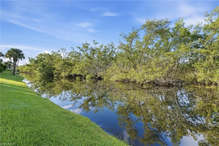 Manicured grassy bank along a water canal, bordered by lush green foliage and mature trees